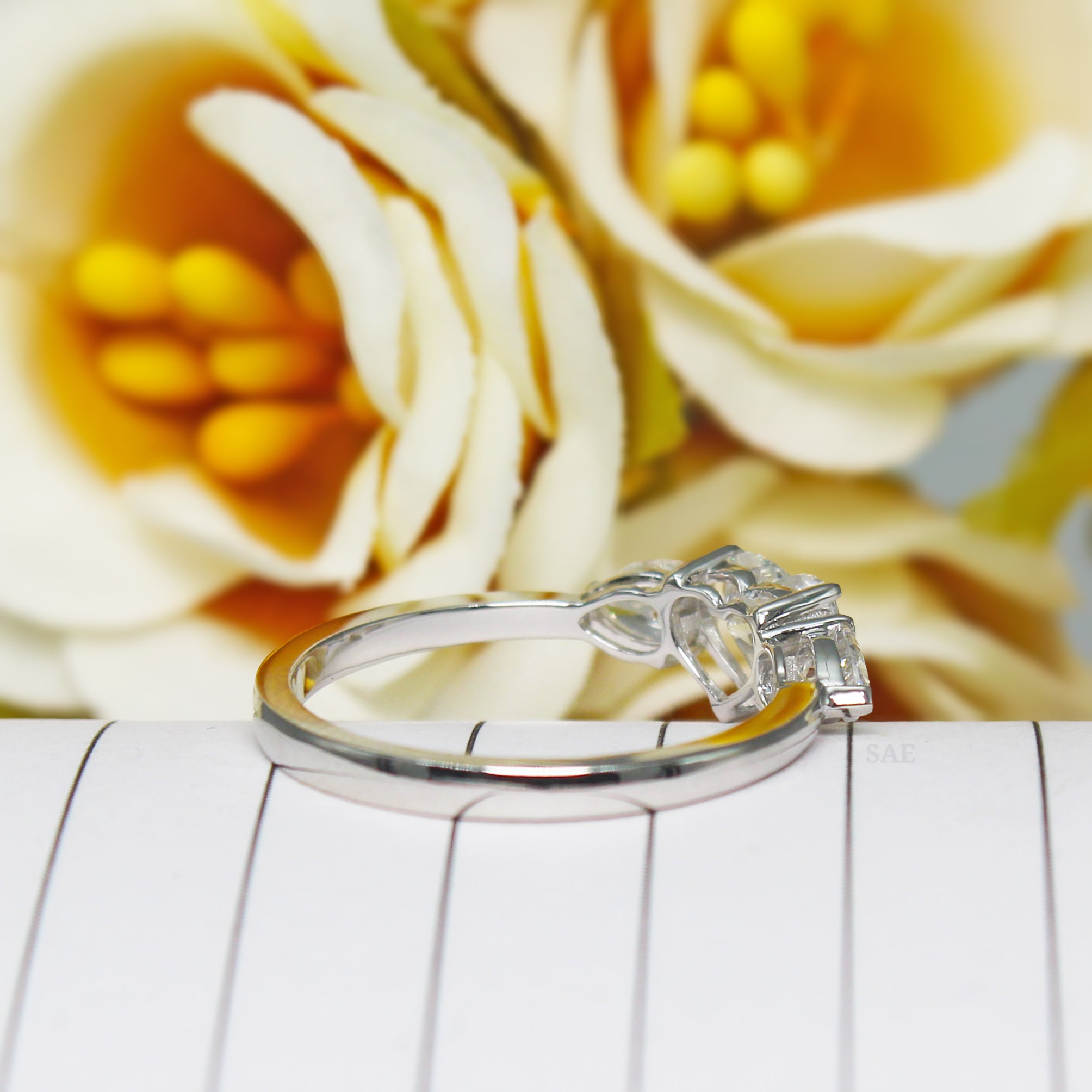 Silver ring with floral design on a white surface with yellow flowers in the background