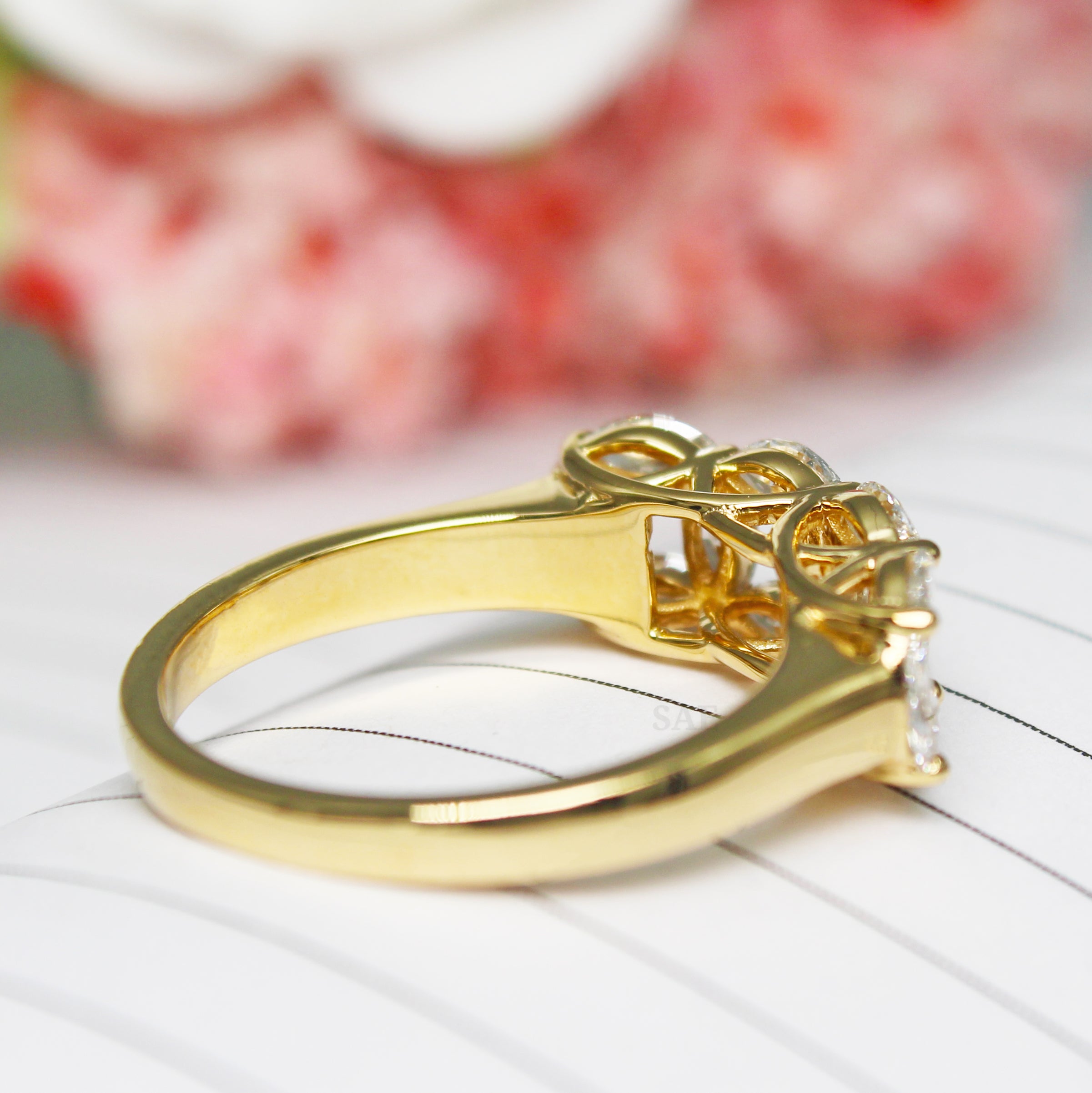 Gold ring with diamond on a white surface with blurred red flowers in the background